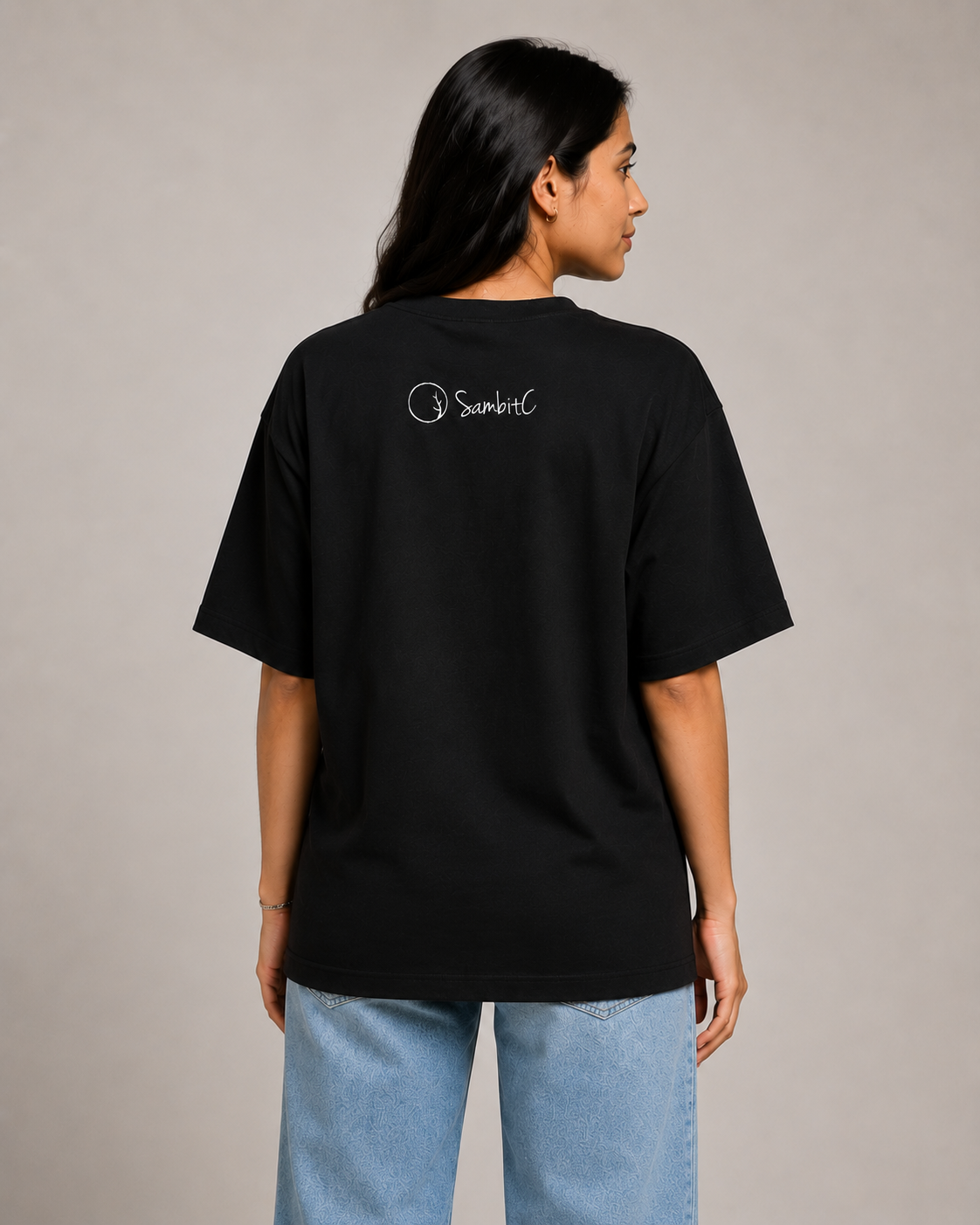 A Female Model wearing a black t-shirt with a logo on the back against a plain background